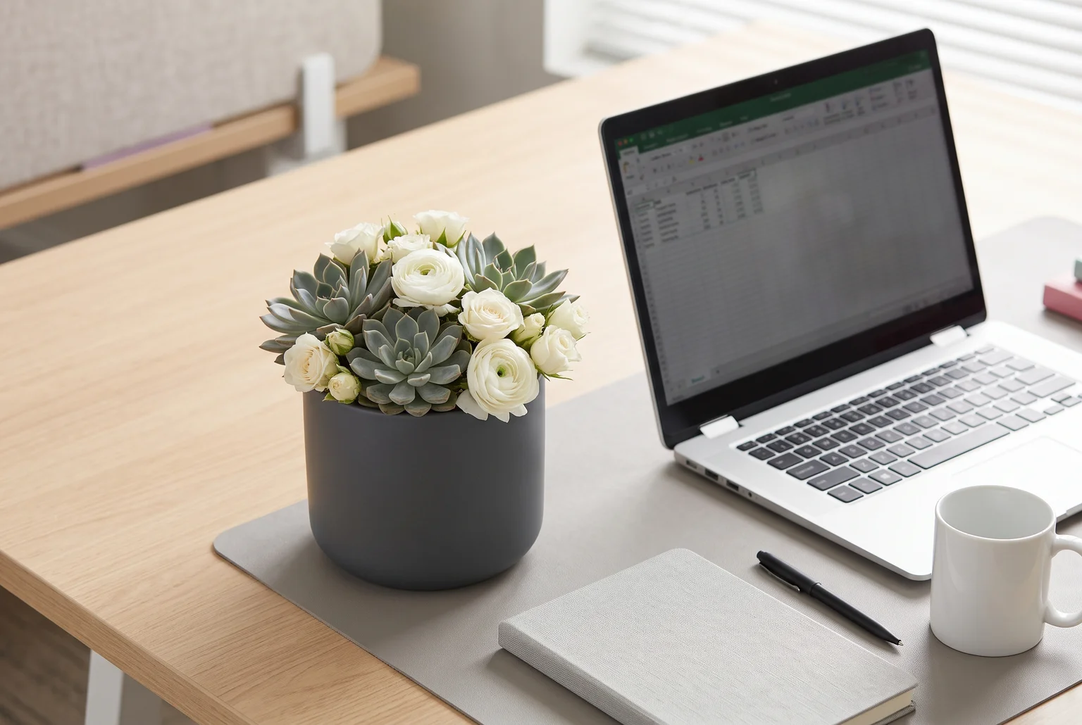 A muted succulent and white bloom arrangement reads as polished and professional, never overdone, right next to the everyday tools of a workday.